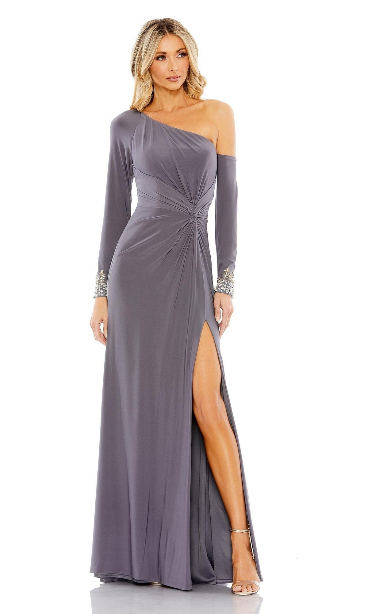 A woman in the Long Formal Dress 12489 by Mac Duggal—a gray, floor-length, one-shoulder gown with a thigh-high slit, long sleeve, and embellished wrist—offers an elegant update to the classic one-shoulder style.